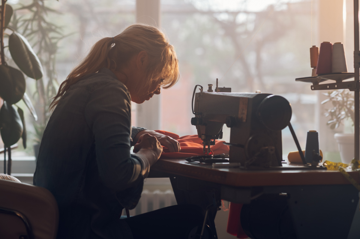 Tailor Woman Sitting And Sewing On A Sewing Machine A In Studio Tailor Woman Sitting And Sewing On A Sewing Machine A In Studio